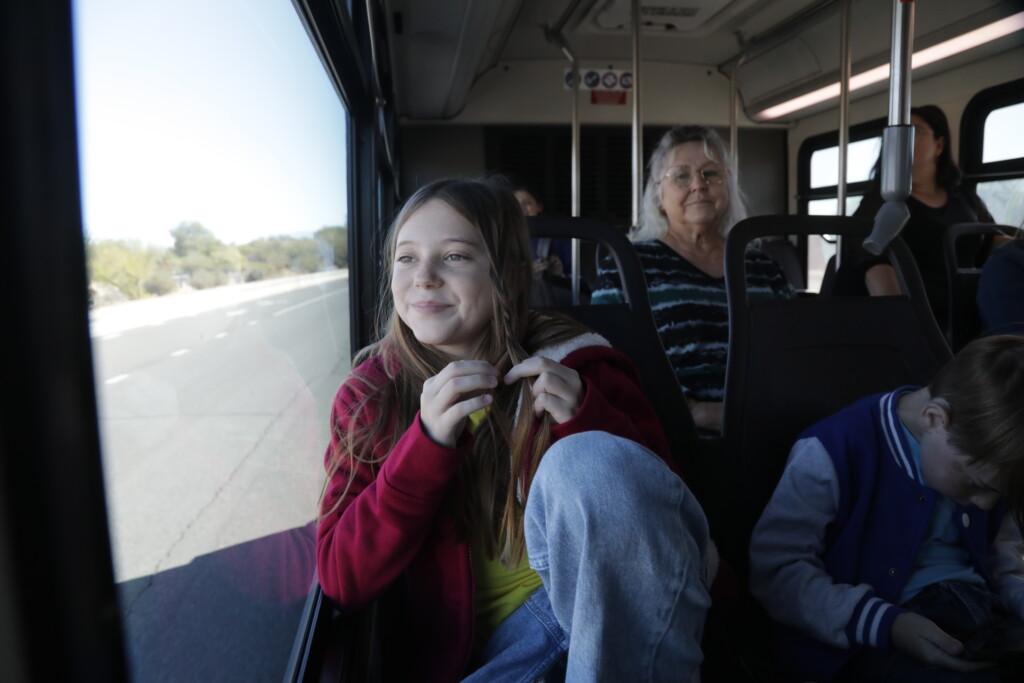 child riding sun tran bus looking out the window with a smile