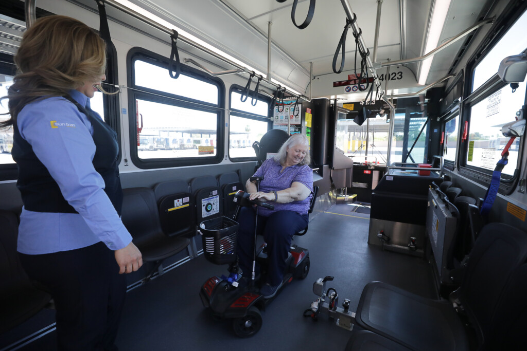 riders with mobility device on bus with driver helping